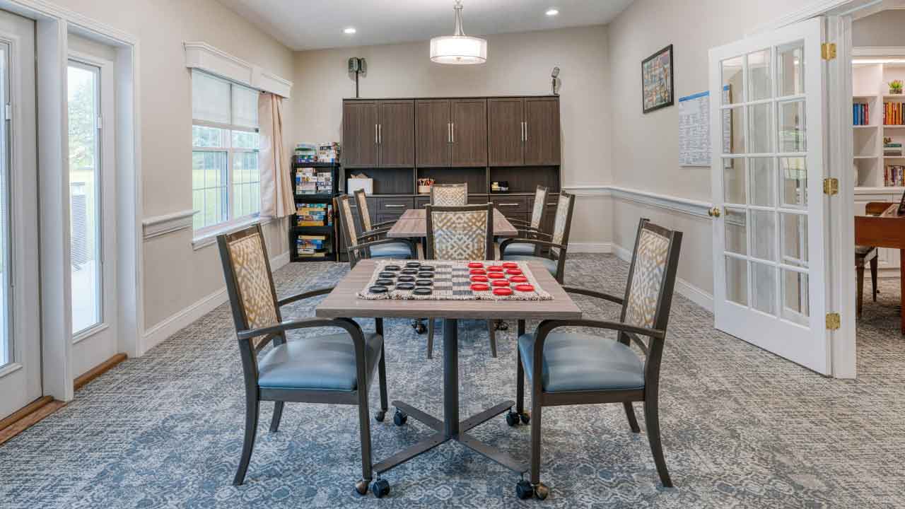 A community room featuring multiple square tables set for games, surrounded by chairs with patterned cushions.