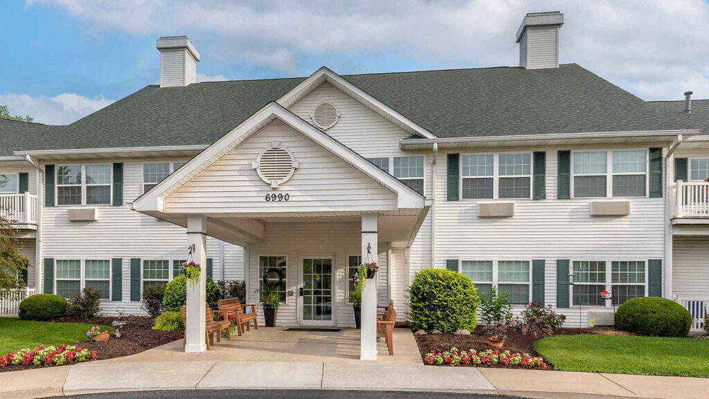 Two-story residential building with white siding, dark green shutters, and a covered entryway marked with the number 6990.