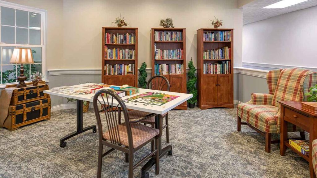 A puzzle room with three wooden bookcases, a central table with a jigsaw puzzle, and a plaid wingback chair.