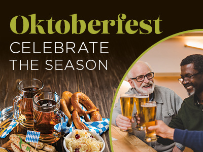 Two men clink beer glasses while smiling at a table with pretzels, sausages, and beer mugs. Text reads: “Oktoberfest. Celebrate the season.”.