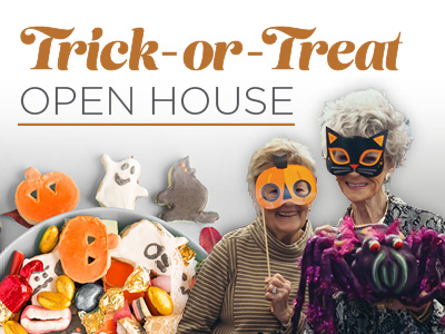 Two older women in Halloween costumes hold candy and a large spider prop, with a bowl of assorted Halloween treats in front. Text above reads “Trick-or-Treat Open House.”.