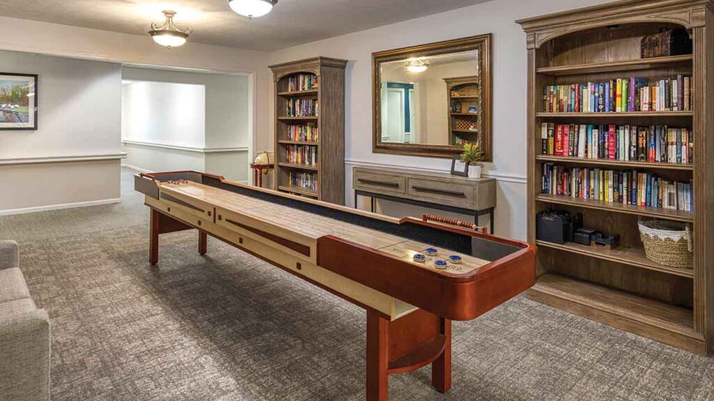 A shuffleboard table sits in the center of a room with two large wooden bookcases filled with books.