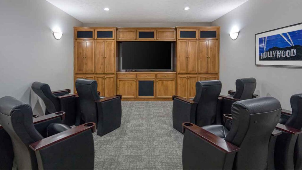 A home theater room with two rows of dark leather recliners facing a large television built into a wooden cabinet, with a Hollywood sign print on the wall.