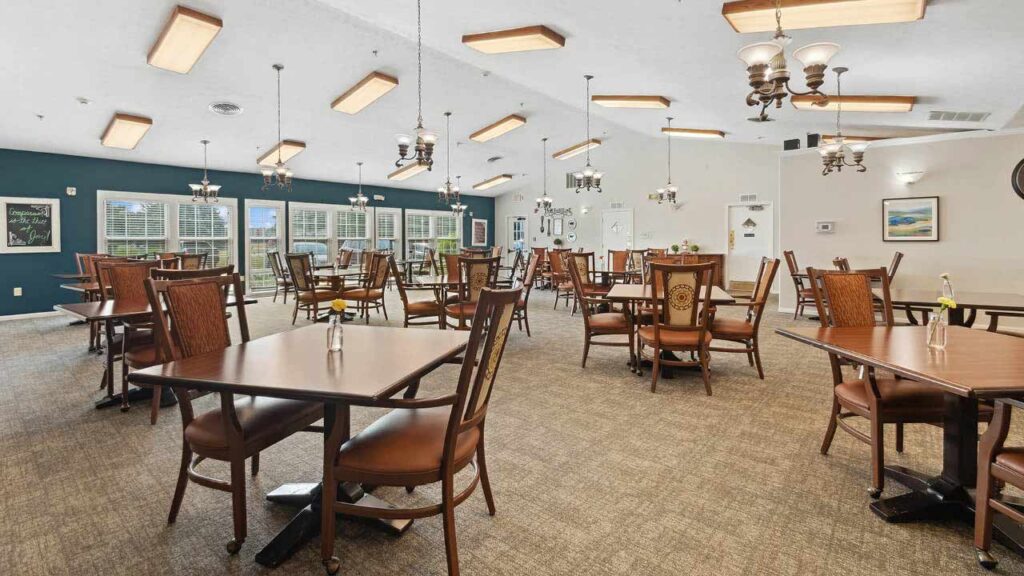 Spacious dining room with wooden tables and chairs, large windows, blue accent wall, chandeliers, and framed art on the walls. Bright, clean, and neatly arranged for guests.