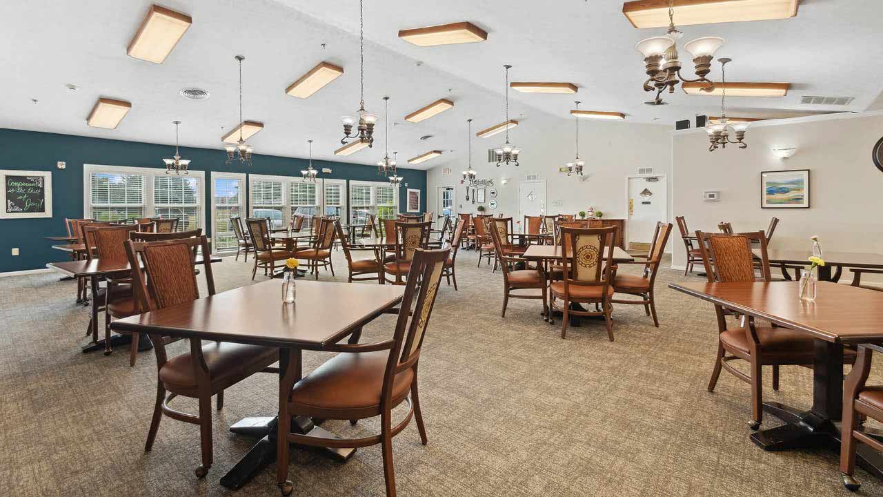 Spacious dining room with wooden tables and chairs, large windows, blue accent wall, chandeliers, and framed art on the walls. Bright, clean, and neatly arranged for guests.