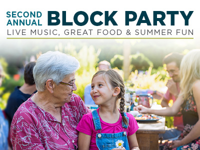An older woman and a young girl smile at each other at an outdoor gathering. Text reads: "Second Annual Block Party. Live Music, Great Food & Summer Fun." Other people are visible enjoying the event in the background.