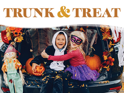 Two children in Halloween costumes sit in the open trunk of a car decorated with fall leaves, pumpkins, and a scarecrow, with the text “TRUNK & TREAT” above them.