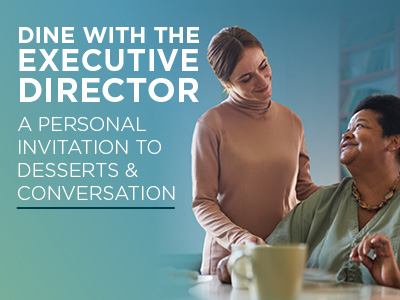 A smiling woman sits at a table with a cup while another woman stands beside her, smiling and touching her shoulder. Text invites people to dine with the executive director for desserts and conversation.