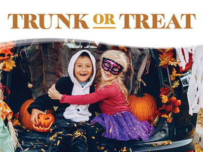 Two smiling children in Halloween costumes sit in a decorated car trunk with pumpkins, autumn leaves, and a jack-o’-lantern. The words “Trunk or Treat” are displayed above them.