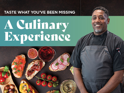 A smiling chef in a dark uniform stands beside a table with assorted gourmet appetizers, drinks, and fruits. Text reads,