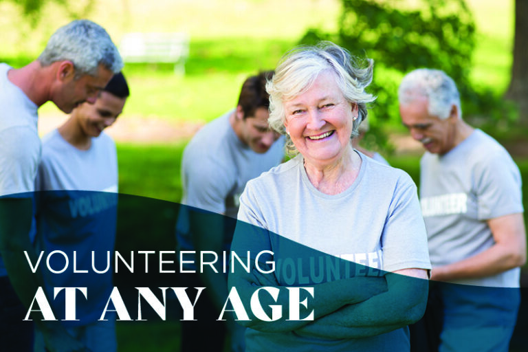 A smiling older woman in a gray โvolunteerโ shirt stands in front of a group of diverse adults outdoors, with the text โVolunteering at any ageโ overlayed on the image.