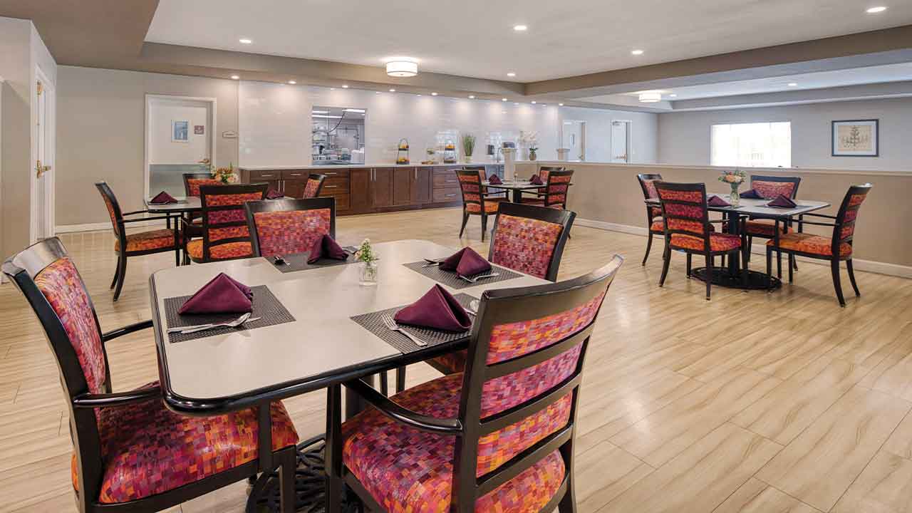 Dining area with several square tables and chairs featuring patterned orange and purple upholstery.