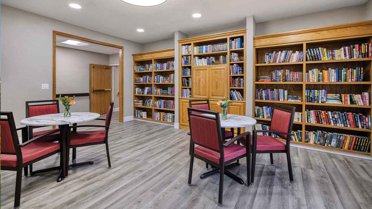 Two small tables with chairs in a library lounge with full bookshelves along the back walls.