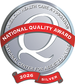Silver medal-style badge reading "American Health Care Association, National Center for Assisted Living," with a red banner saying "National Quality Award" and "2026 Silver" at the bottom—an esteemed recognition of excellence in senior living.