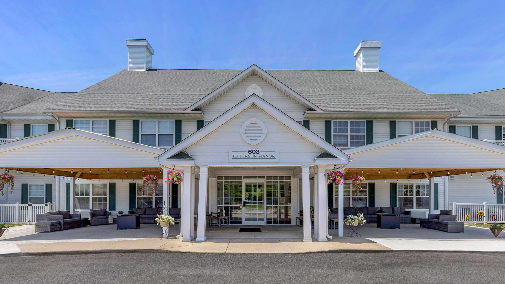Stately traditional senior living building with a large front lawn, green shutters, and a covered entrance at Jefferson Manor in Kokomo, IN, Howard County.