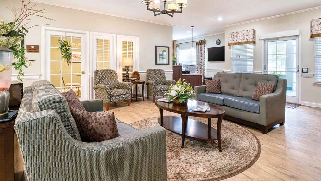 A furnished lounge area featuring two patterned armchairs, a gray sofa, a wooden coffee table, and a circular rug on light wood flooring.